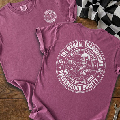Maroon t-shirt with a skeleton driving a manual transmission graphic and text.