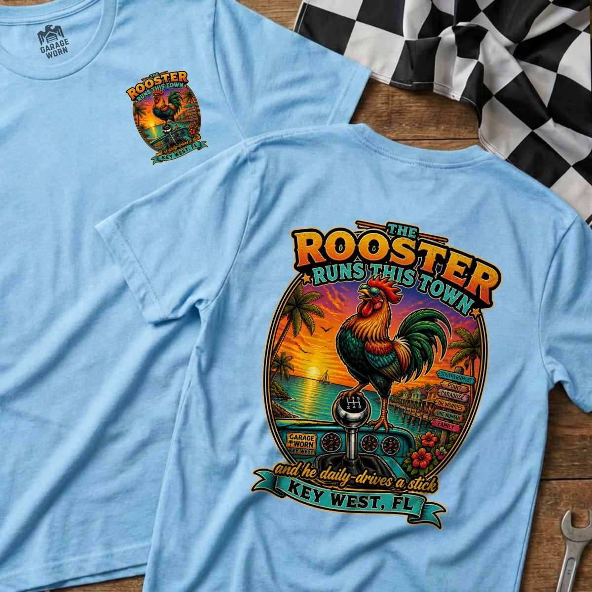 Light blue t-shirt with a graphic of a rooster on a gear shift, Key West scene, and text.