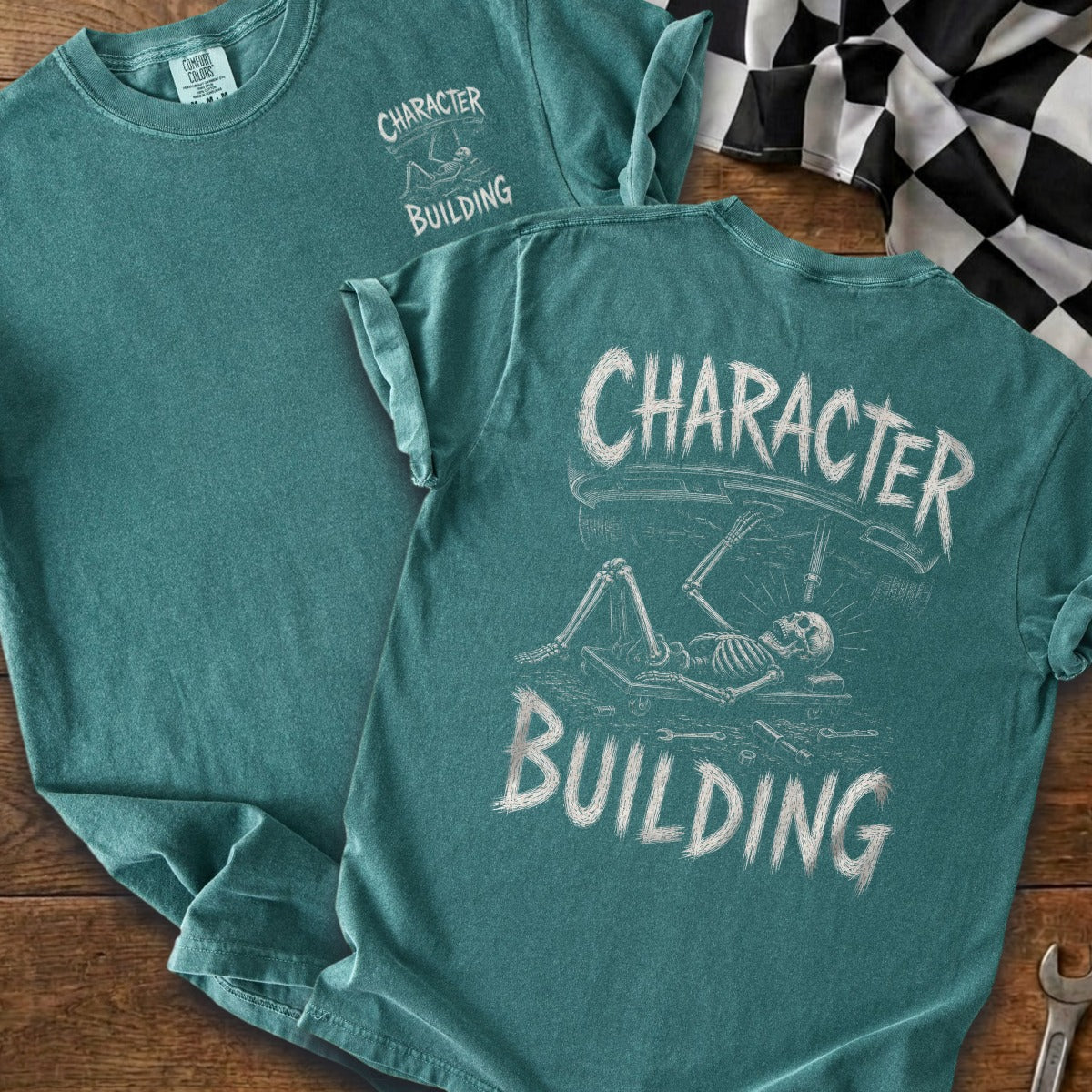 Teal t-shirt with skeleton working on car graphic and text "CHARACTER BUILDING."
