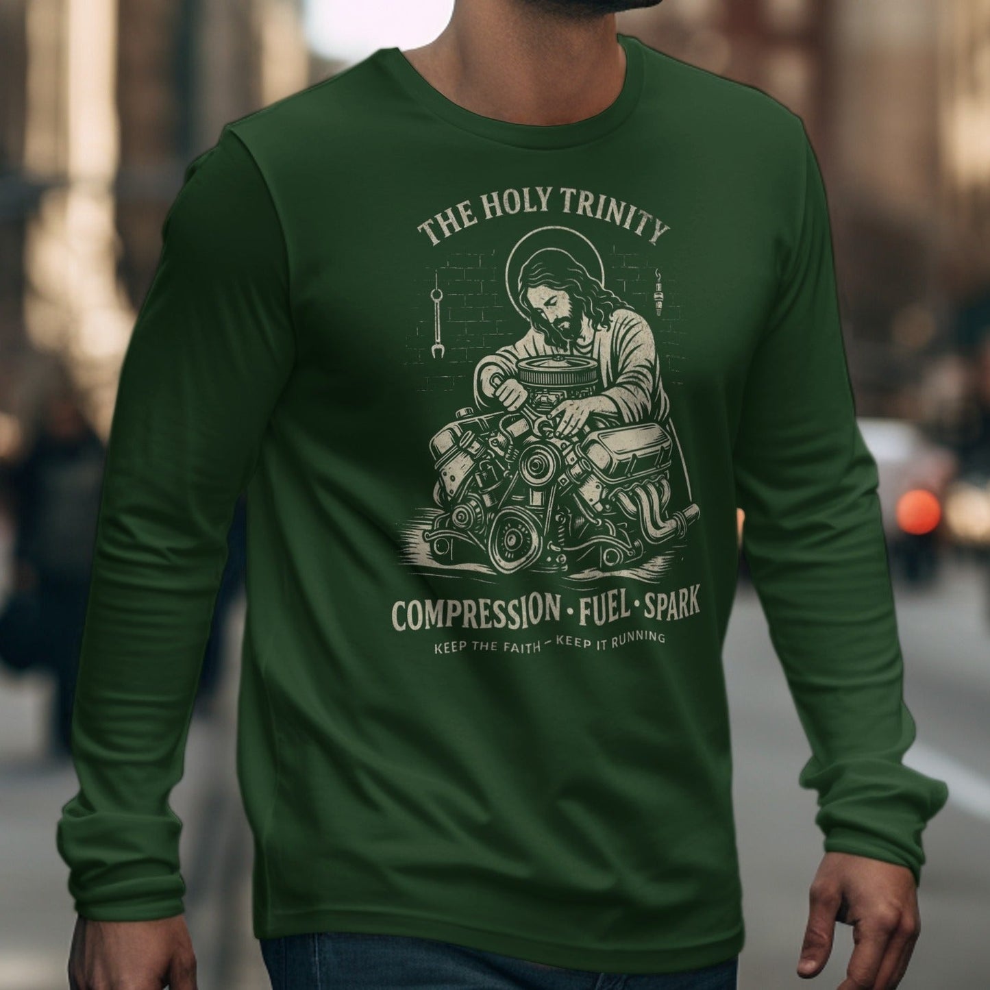 Green long-sleeve shirt with Jesus working on an engine graphic and "The Holy Trinity" text.
