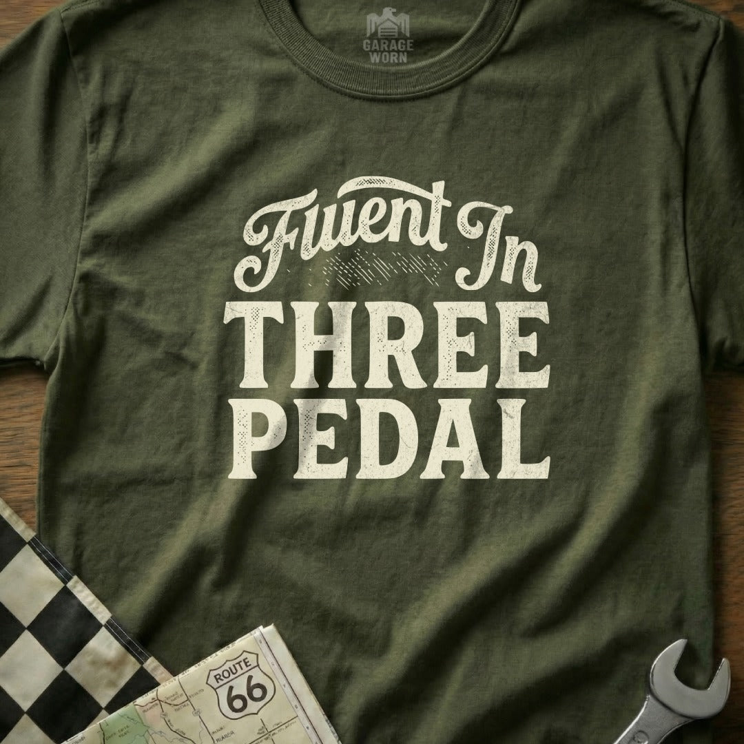 Green t-shirt with "Fluent In Three Pedal" text and checkered flag detail.