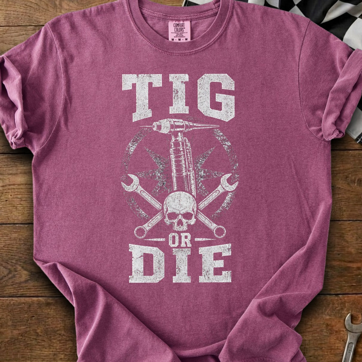 TIG OR DIE text with skull, welder, and wrenches graphic on a maroon t-shirt.