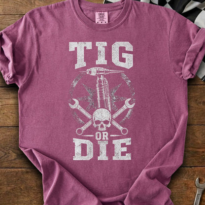 TIG OR DIE text with skull, welder, and wrenches graphic on a maroon t-shirt.