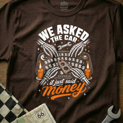 Brown t-shirt with skeletal hands on a Ouija board, saying "We Asked the Car, it Just Said Money."