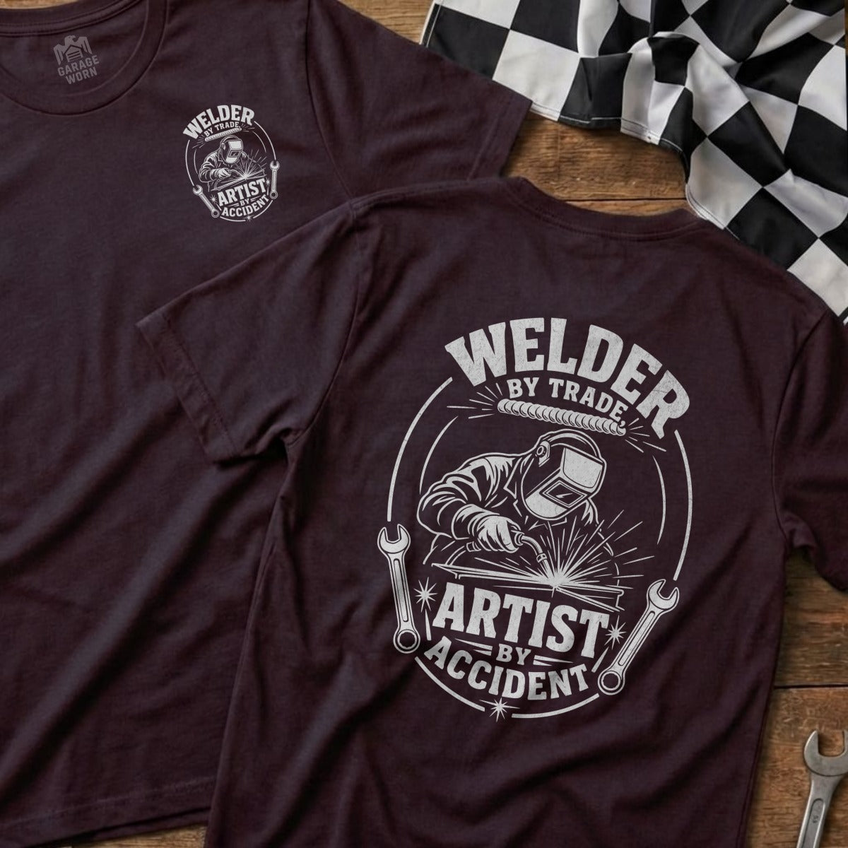 Dark maroon t-shirt with "Welder by Trade, Artist by Accident" graphic.