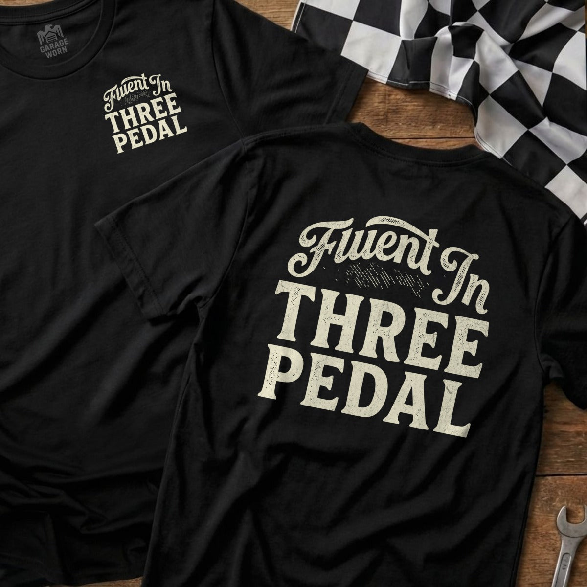 Black t-shirt with "Fluent In Three Pedal" text on back, with a checkered flag.