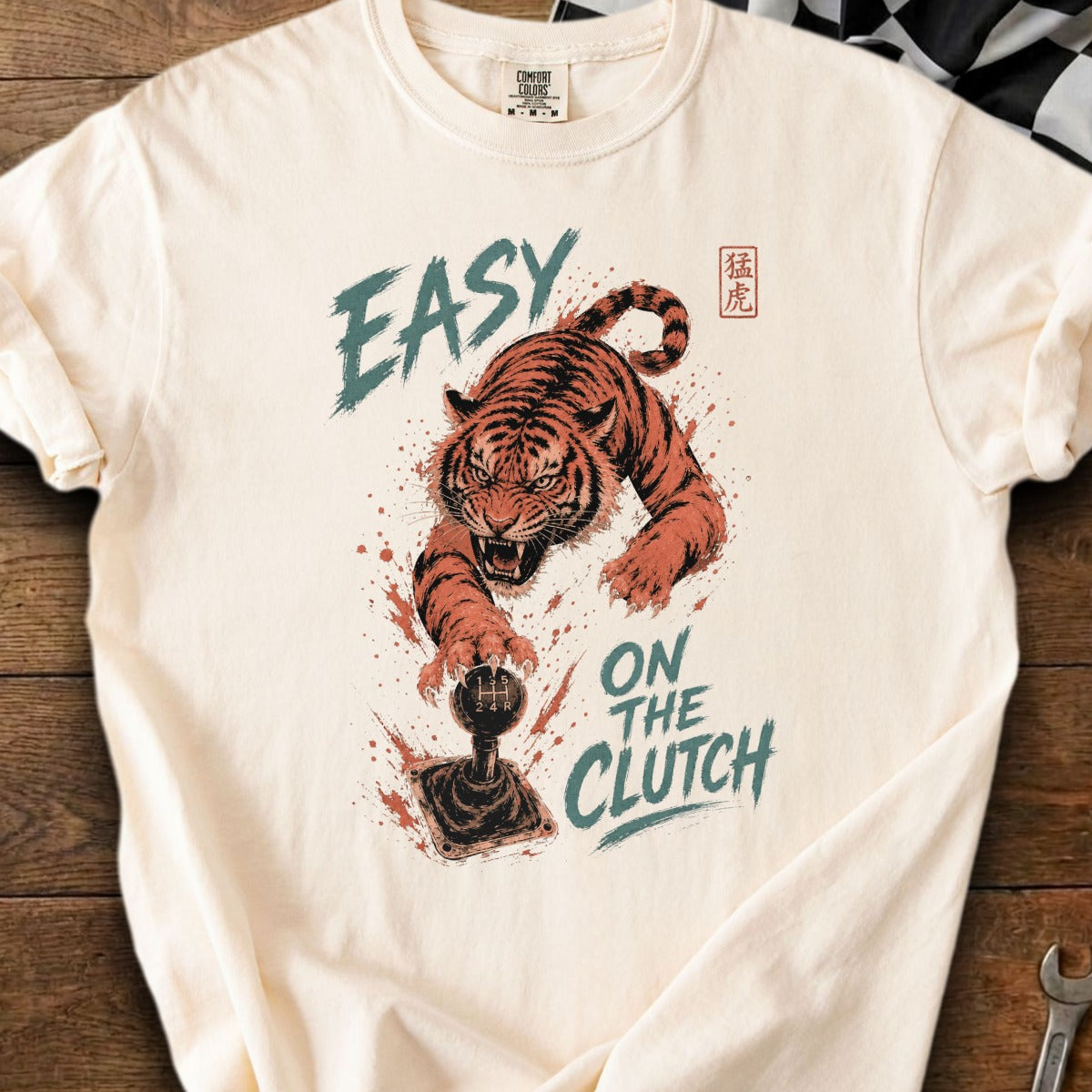 Cream t-shirt with aggressive tiger reaching for a gear shift, text reads "EASY ON THE CLUTCH".