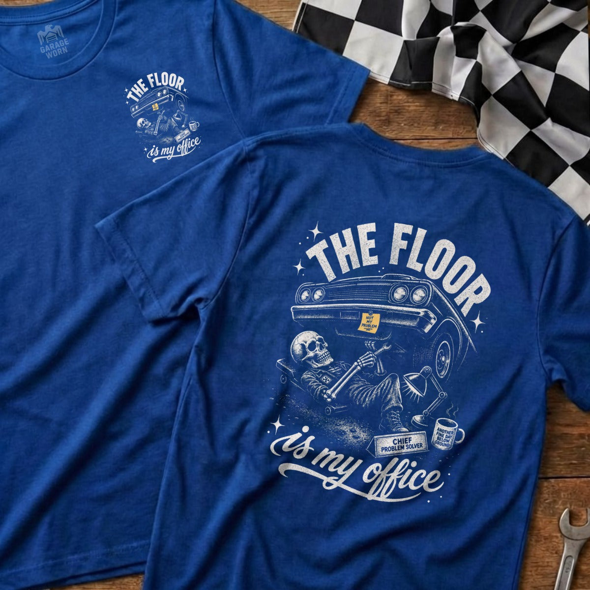 Blue t-shirt with distressed graphic of skeleton working on car, "The Floor is My Office."