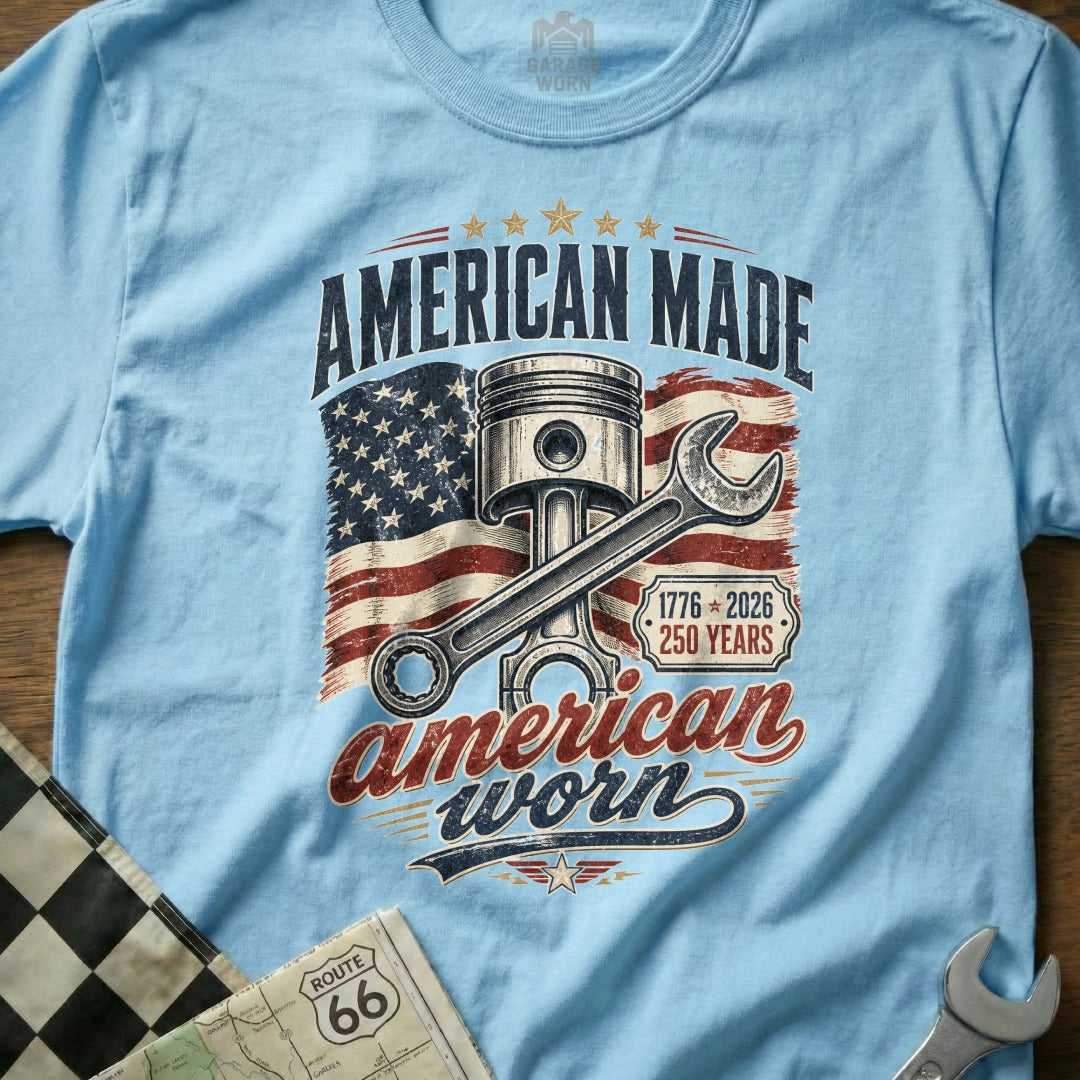 Light blue t-shirt with American flag, piston, wrench, and text "American Made American Worn".