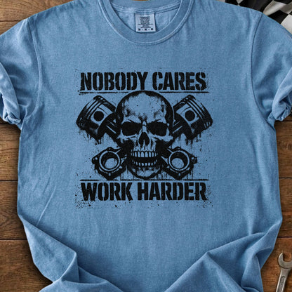 Blue t-shirt with black graphic of skull and pistons, text reads "NOBODY CARES WORK HARDER".