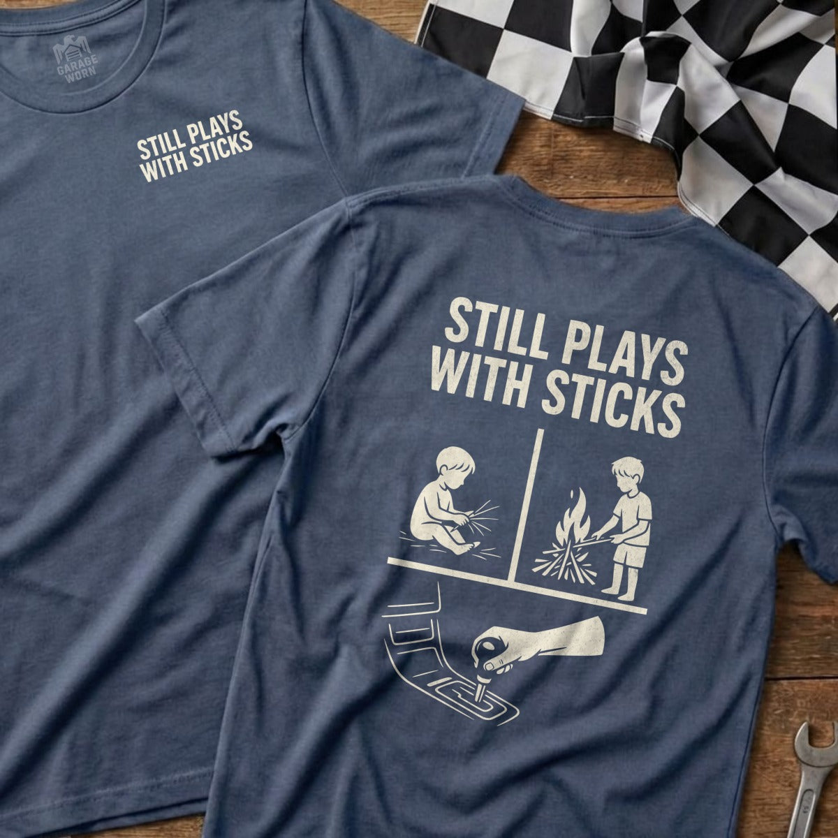 T-shirt with "Still Plays With Sticks" text and graphics of controller and campfire.