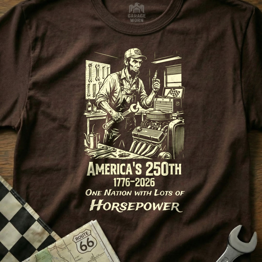 Brown t-shirt with a mechanic and text "America's 250th 1776-2026 One Nation With Lots of Horsepower".
