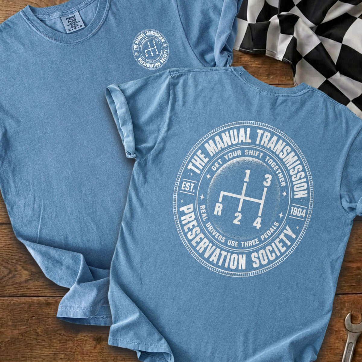Blue t-shirt with white Manual Transmission Preservation Society graphic and a gear shift pattern.