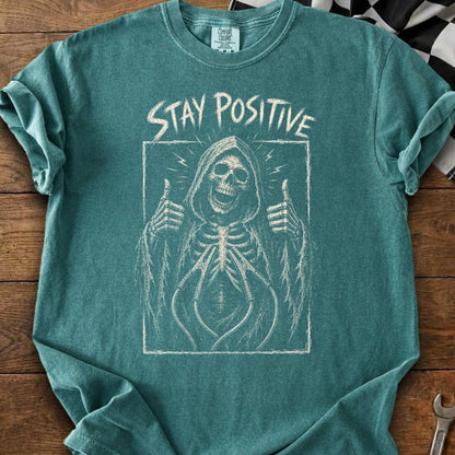 Teal t-shirt with grim reaper skeleton giving thumbs up and "Stay Positive" text.