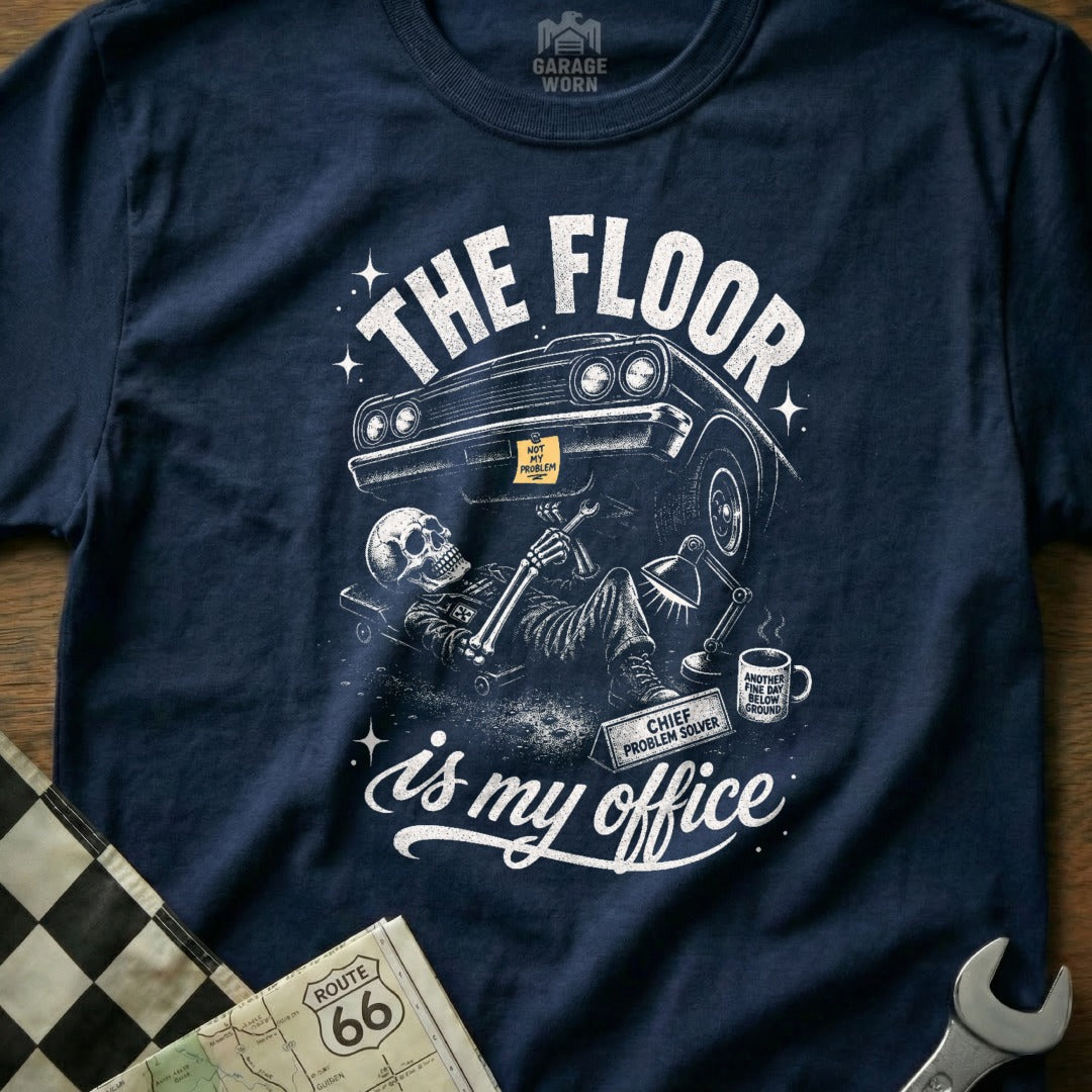 Navy t-shirt with skeleton mechanic fixing car, text "The floor is my office."