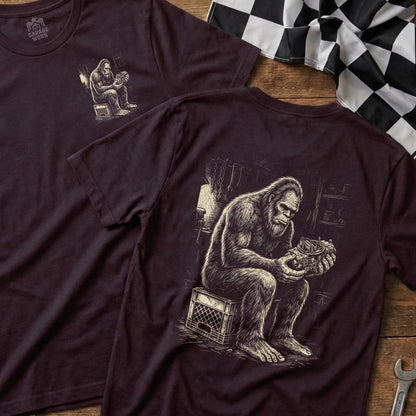 T-shirt with Bigfoot sitting on a crate, holding a carburetor.