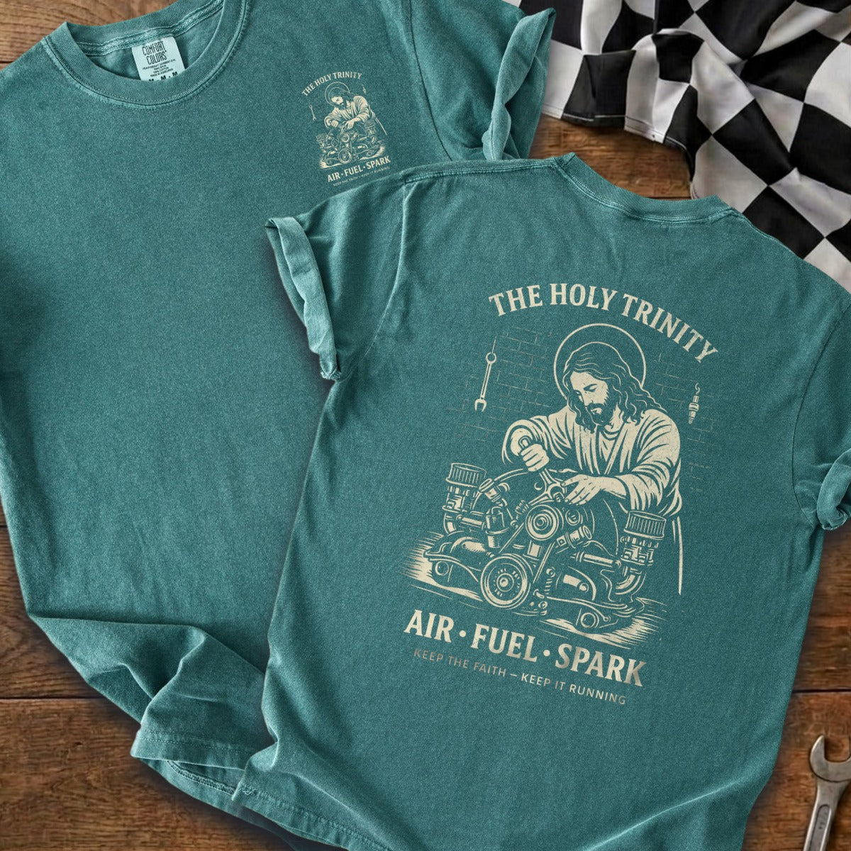 Dark teal t-shirt with Jesus working on an engine graphic and text "The Holy Trinity Air Fuel Spark".