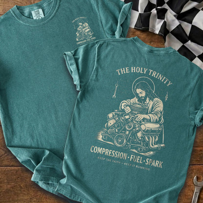 Teal t-shirt with graphic of Jesus working on an engine, "The Holy Trinity," and "Compression Fuel Spark."