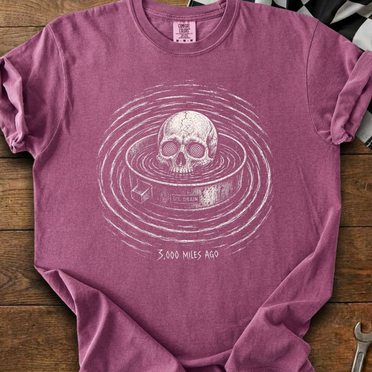 Skull in oil drain with "3,000 Miles Ago" text on maroon t-shirt.