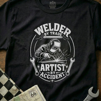 Welder by trade, artist by accident graphic on a black t-shirt.