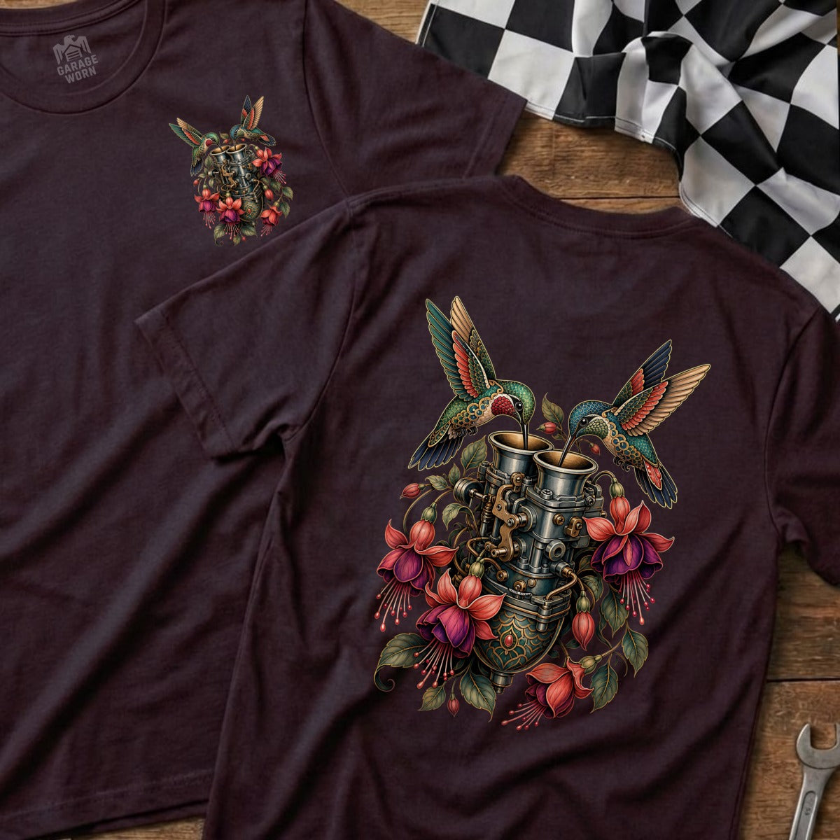 Two hummingbirds feed from a carburetor adorned with fuchsia flowers on a maroon t-shirt.