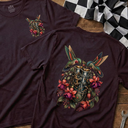 Two hummingbirds feed from a carburetor adorned with fuchsia flowers on a maroon t-shirt.