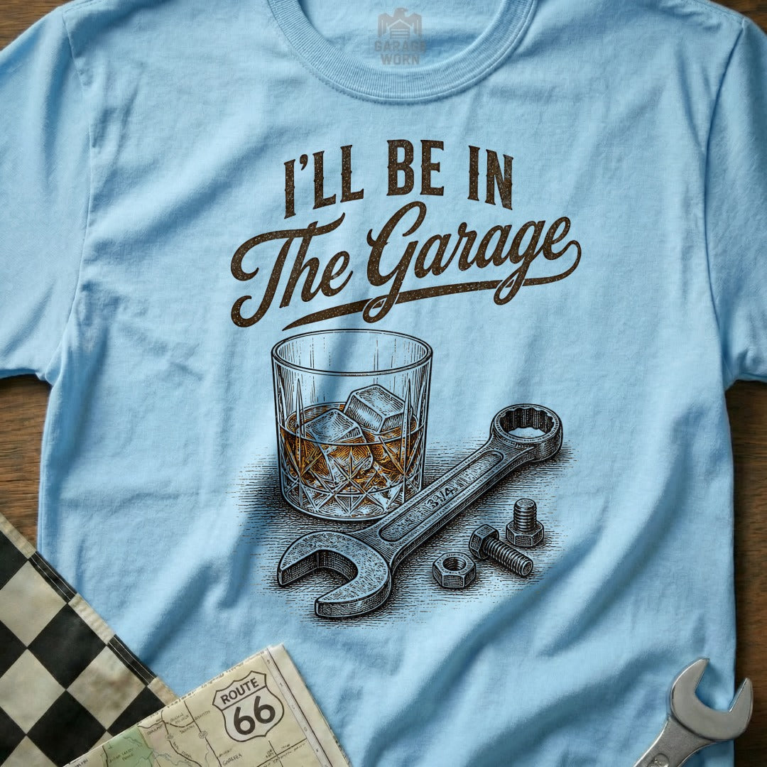 Light blue t-shirt with "I'll Be In The Garage" text, a glass of whiskey, and tools.