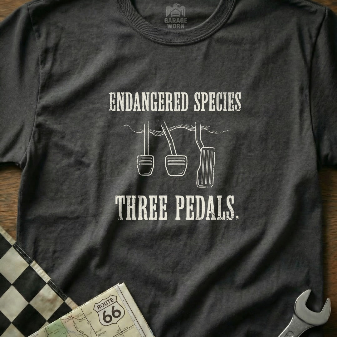 T-shirt with "Endangered Species Three Pedals" text and clutch, brake, gas pedals graphic.