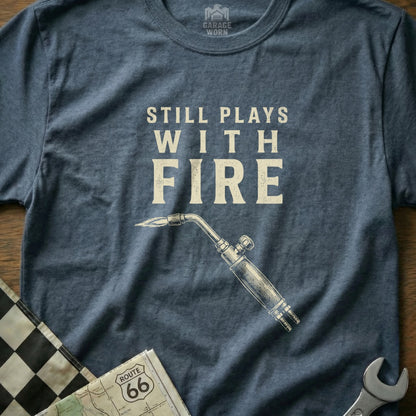 Navy t-shirt with "Still Plays With Fire" and a welding torch graphic.