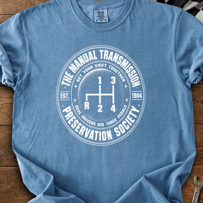 Blue t-shirt with white circular graphic showing a manual gear shift pattern and text.