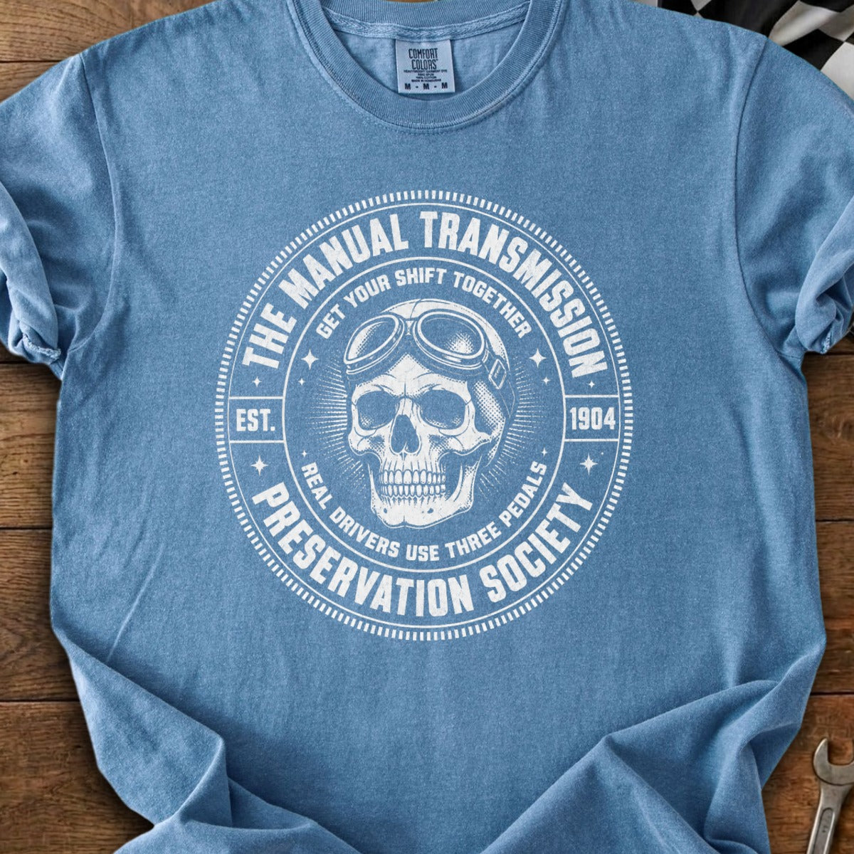 Blue t-shirt graphic: skull with goggles, "The Manual Transmission Preservation Society est. 1904."