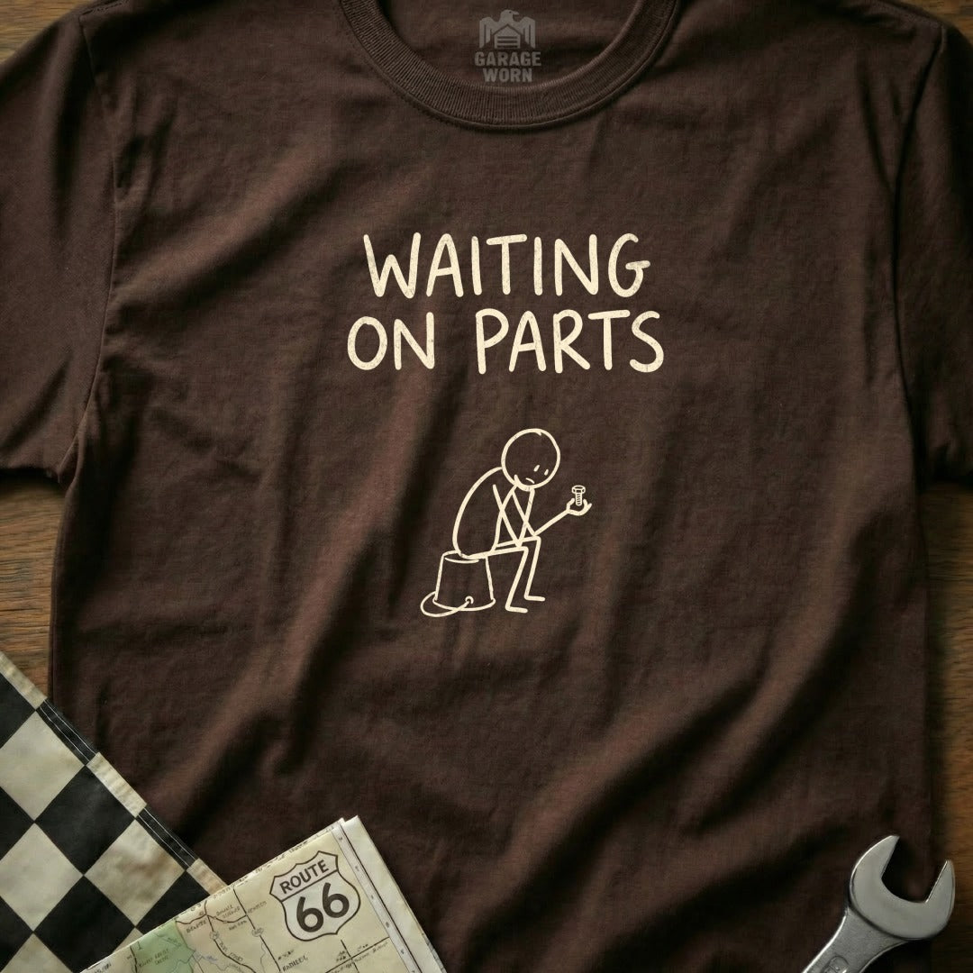 Brown t-shirt with "WAITING ON PARTS" in white text and stick figure holding a bolt.