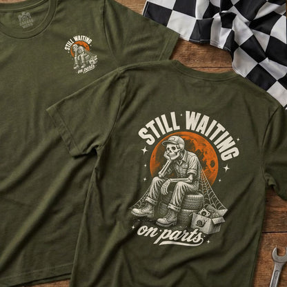 Green t-shirt with graphic of skeleton sitting on tires, text reads "STILL WAITING on parts".