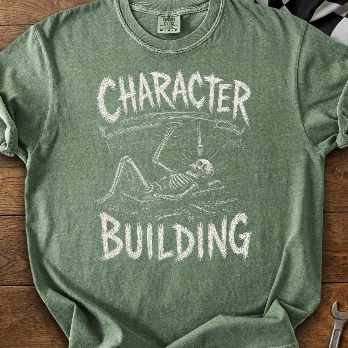 Green t-shirt with skeleton working on a car, text reads "CHARACTER BUILDING".