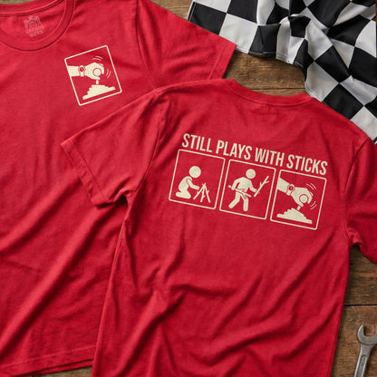 Red t-shirt with "Still Plays With Sticks" and stick figure graphic.