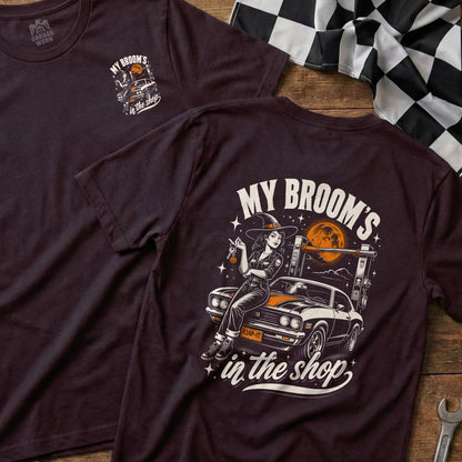 T-shirt graphic of a witch sitting on a car with "My broom's in the shop" text.