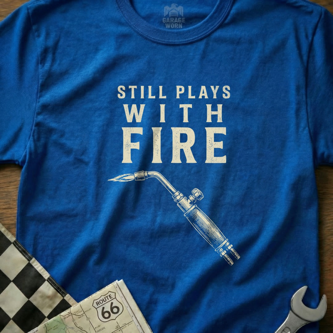 Blue t-shirt with "Still Plays With Fire" text and a welding torch graphic.