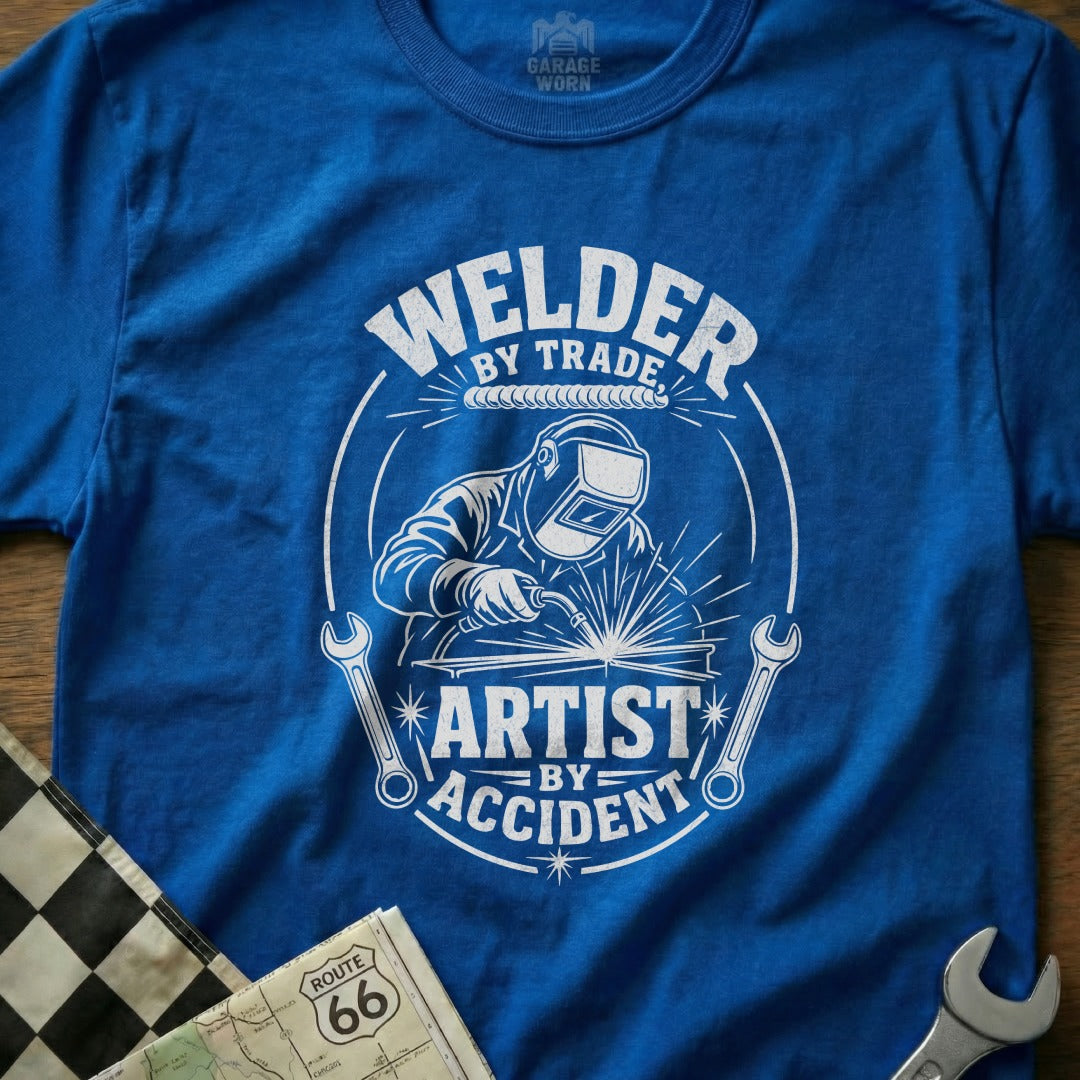 Blue t-shirt with graphic "Welder By Trade, Artist By Accident" and welder illustration.