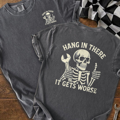 Grey t-shirt with skeleton holding wrench and giving thumbs up, text reads "Hang in there. It gets worse."