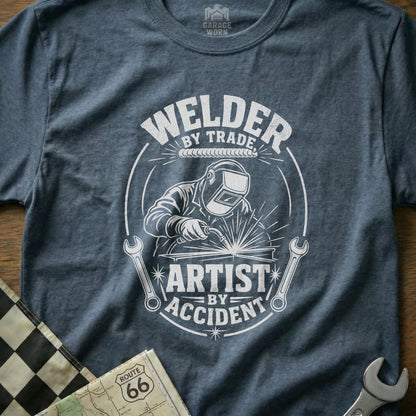 T-shirt with white graphic: "Welder by Trade, Artist by Accident" with welder illustration.