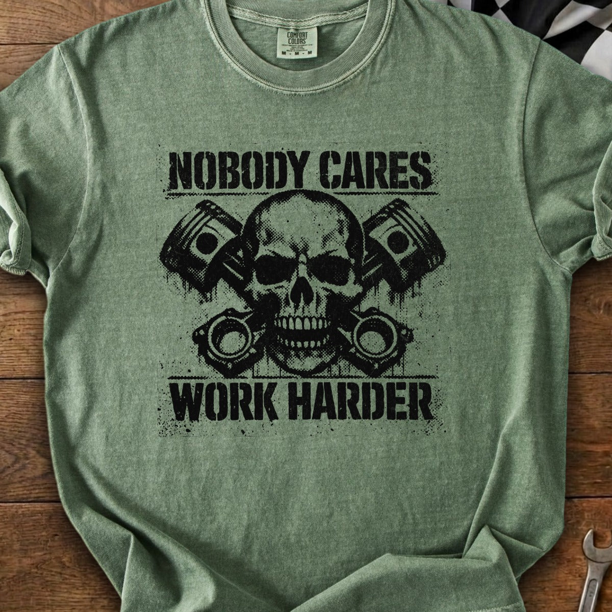 Green t-shirt with black graphic of skull, pistons, and text "NOBODY CARES WORK HARDER".