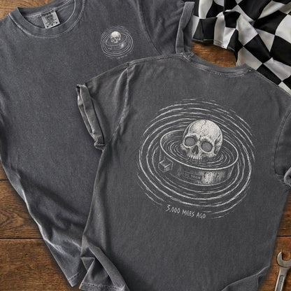 Dark t-shirt with skull in oil drain graphic and text "3,000 Miles Ago".