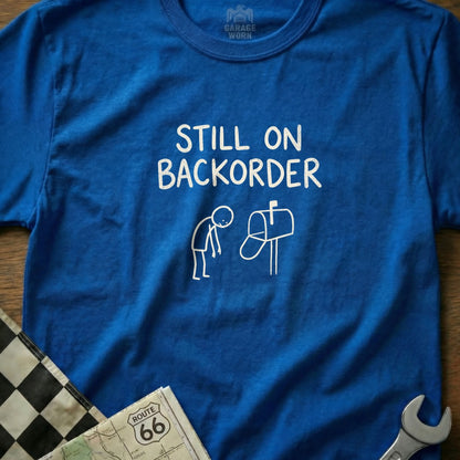 Blue t-shirt with "Still on Backorder" text and a person by a mailbox graphic.