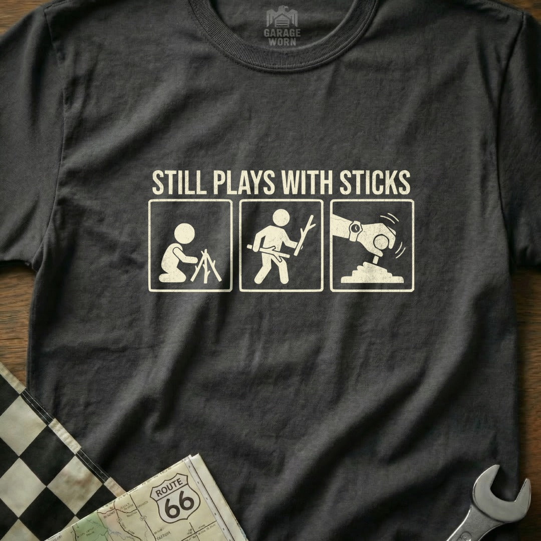 T-shirt graphic showing stick figures transitioning from campfire to playing with sticks and then operating a car gear shift.