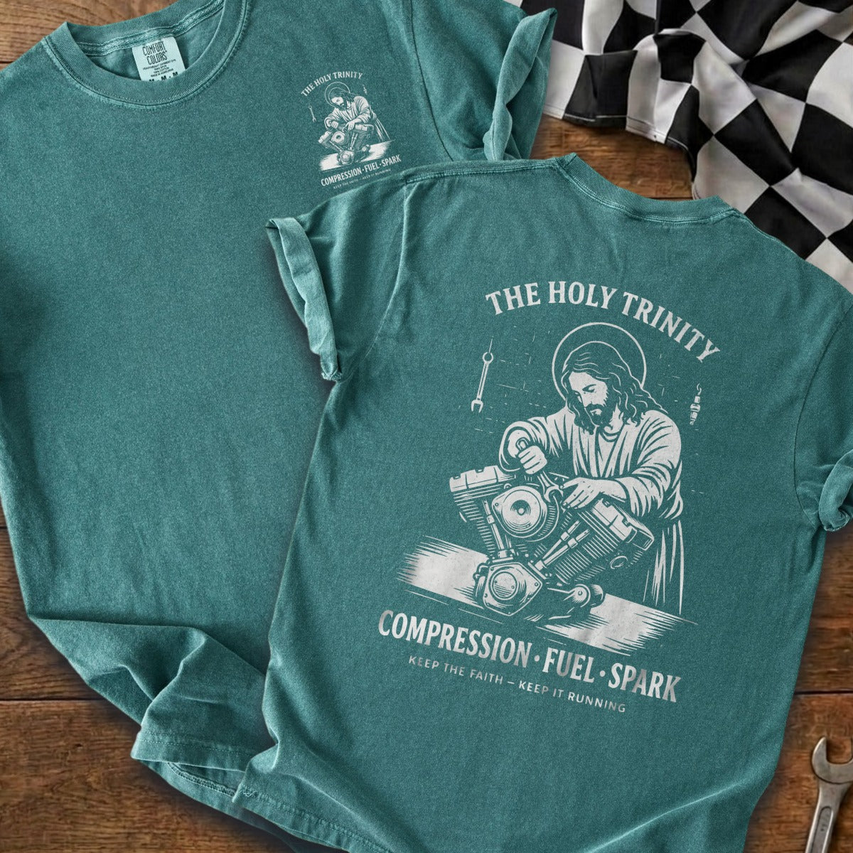 Teal t-shirt features Jesus working on a motorcycle and "The Holy Trinity" text.