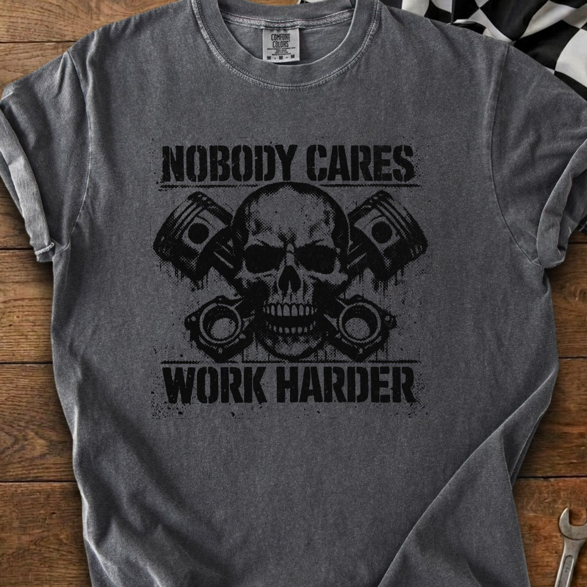 Dark grey t-shirt with black skull, pistons, and text "NOBODY CARES WORK HARDER".
