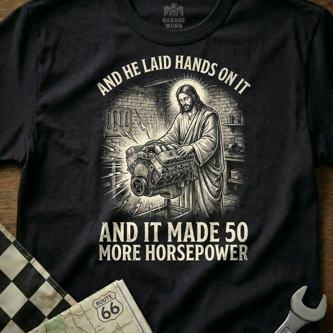 Black t-shirt with Jesus working on an engine, text reads "And he laid hands on it and it made 50 more horsepower."