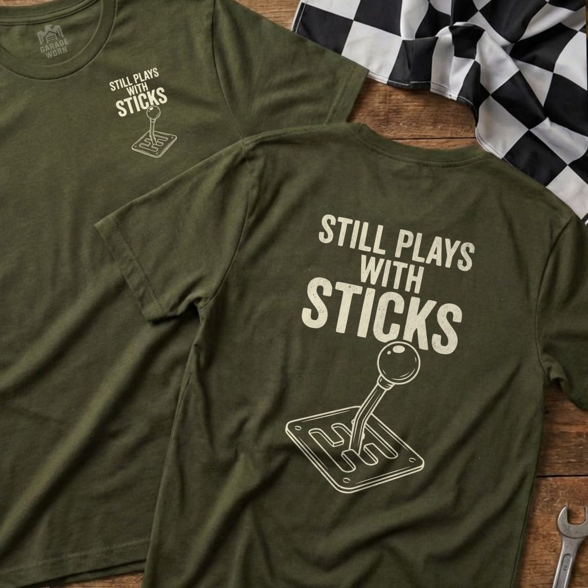 Green t-shirt with "Still Plays With Sticks" and gear shift graphic.