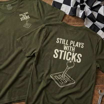 Green t-shirt with "Still Plays With Sticks" and gear shift graphic.
