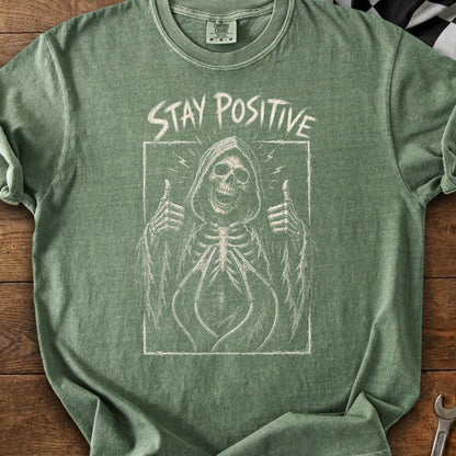 Green t-shirt with a chalk-style graphic of a skeleton giving a thumbs up with "STAY POSITIVE" text.